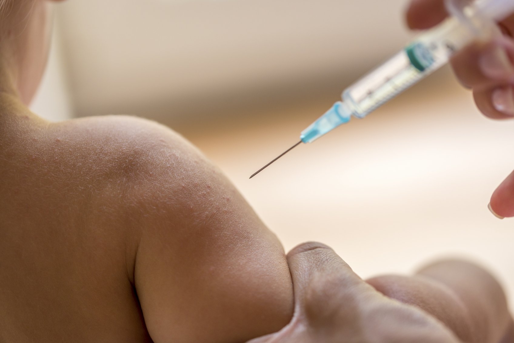 Doctor injecting a young child with a vaccination or antibiotic in a small disposable hypodermic syringe, close up of the kids arm and needle.