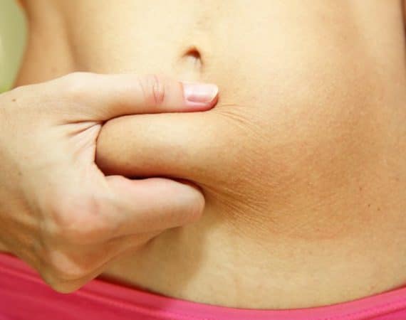 A close-up image of a slim young woman with a belly fat after giving birth. Woman's torso with some belly fat. Abdominal fat.