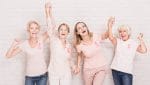 Group of smiling ladies with pink ribbons cheering and holding hands